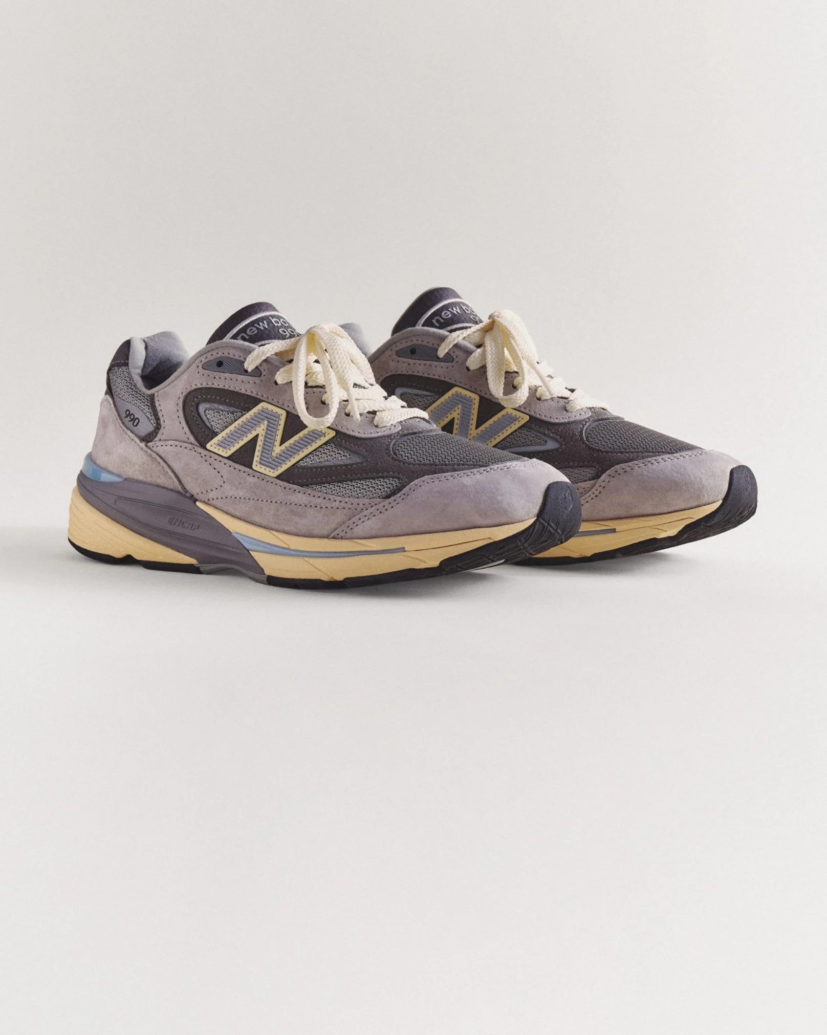 A pair of grey 990v7 sneakers sitting on a grey studio backdrop.