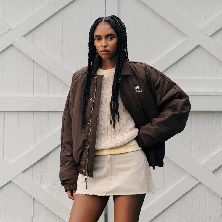 A woman standing in front of a barn wearing a New Balance jacket.