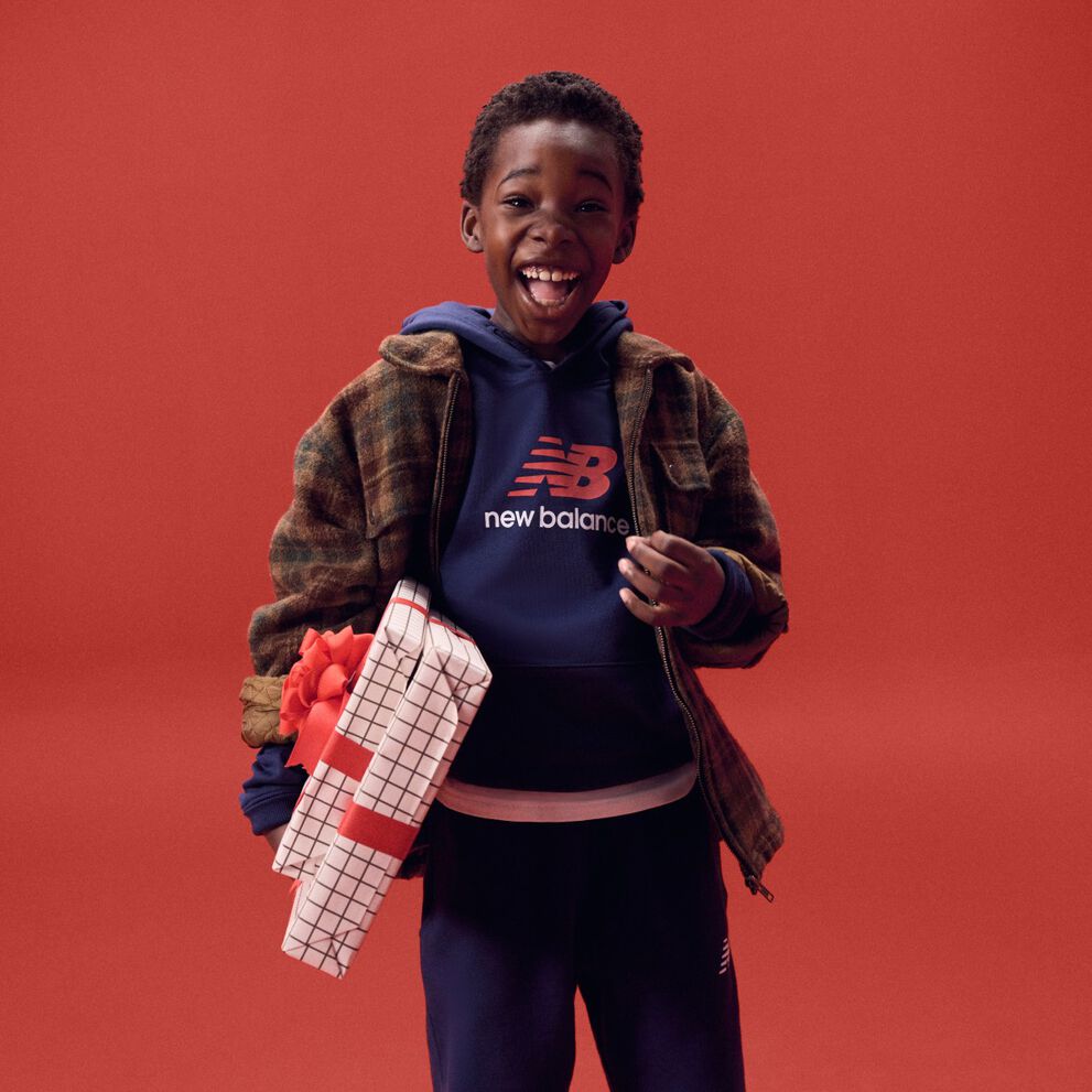 Kid laughing while holding gifts on a red background.