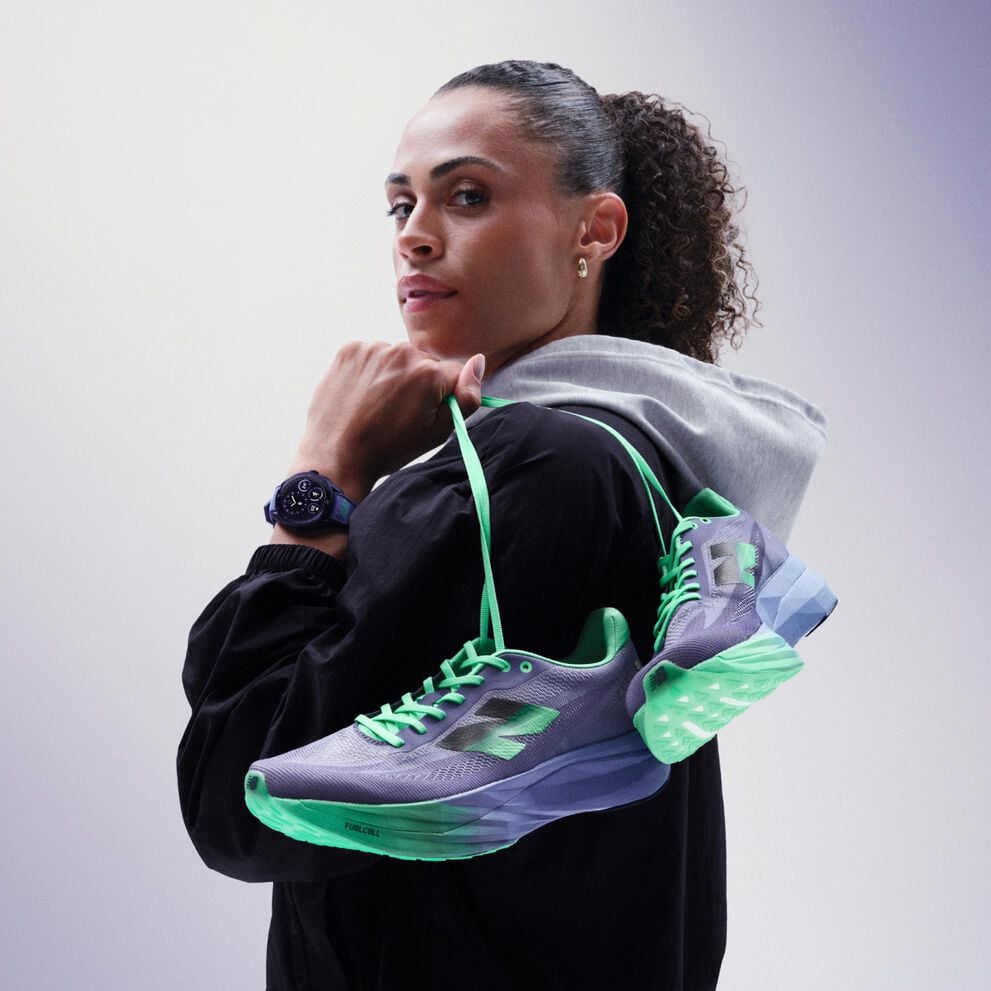  Sydney McLaughlin-Levrone holding a pair of shoes over her shoulder and looking towards the viewer. 