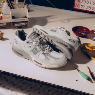 A pair of New Balance Made in UK sneakers in front of a rabbit in a brown textured studio environment. 