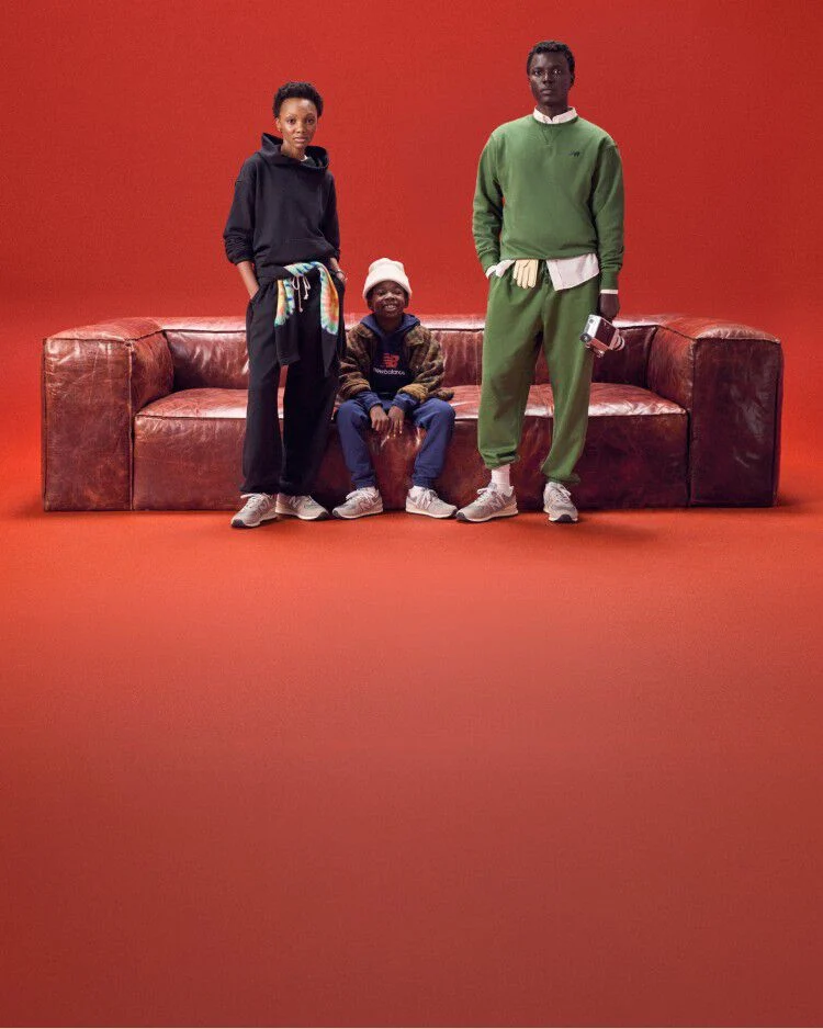 A group of people wearing New Balance standing next to a sofa with a red background.