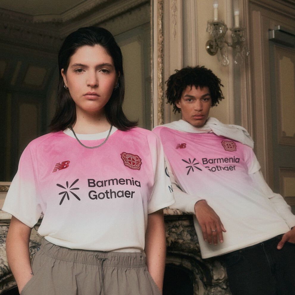 Young couple wearing pink soccer jerseys leaning up against a mirror. 