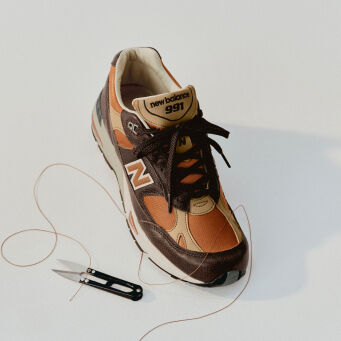 A New Balance Made in UK sneaker in a white studio environment next to sewing thread and fabric shears. 