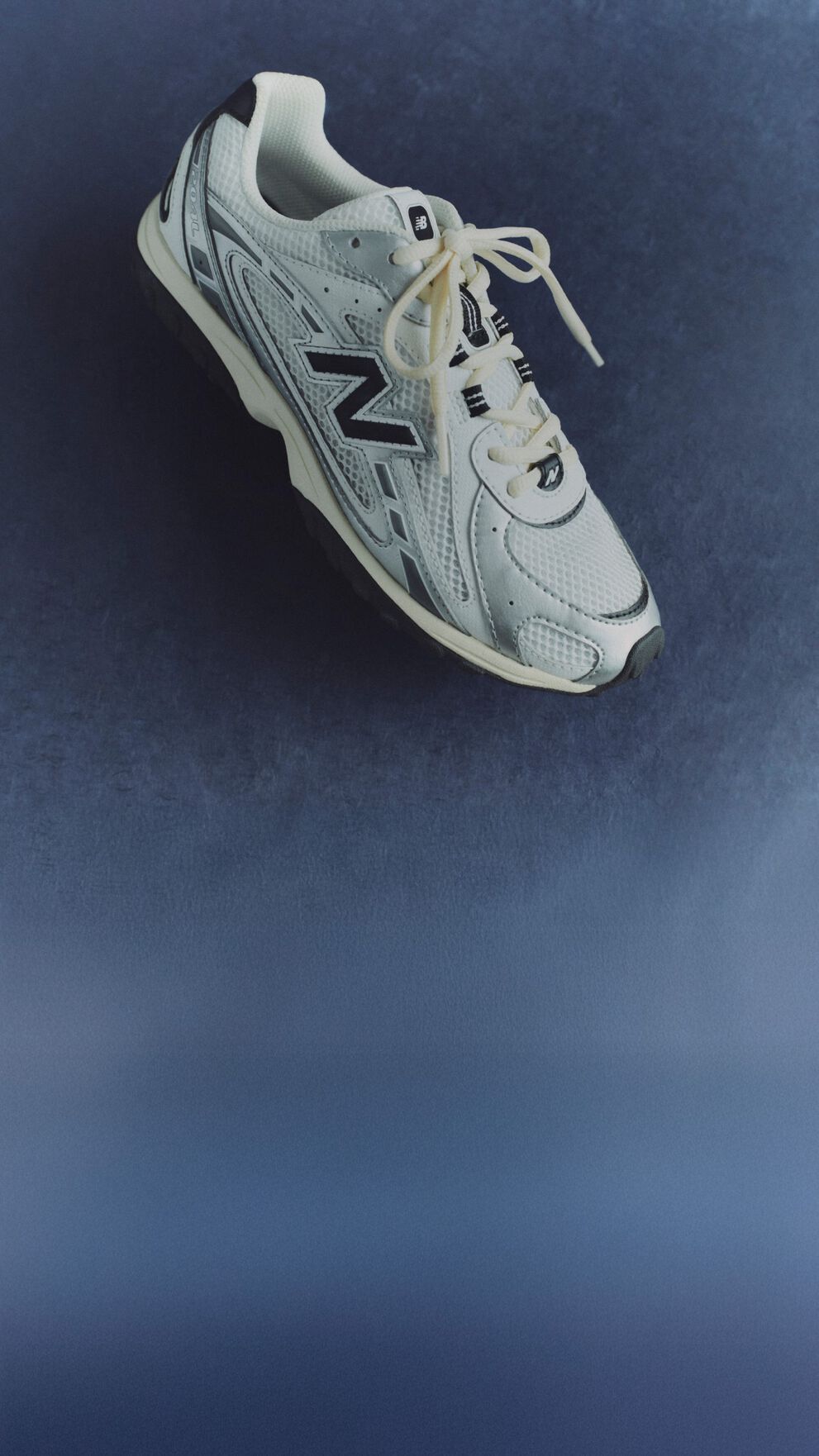 A pair of white and black 204L sneakers against a blue background.