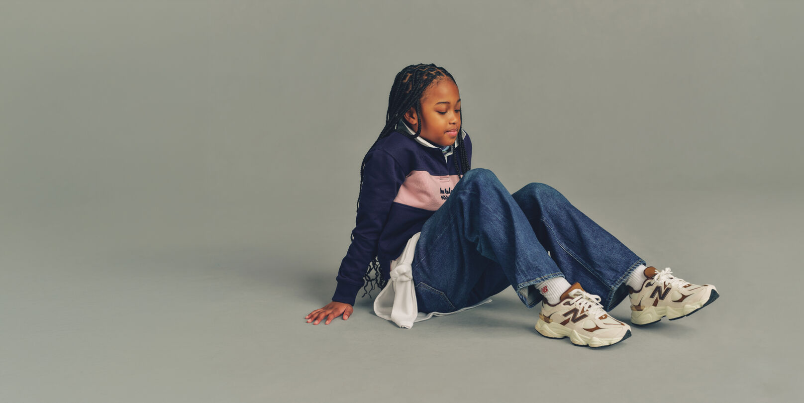 Child sitting on the ground wearing New Balance
